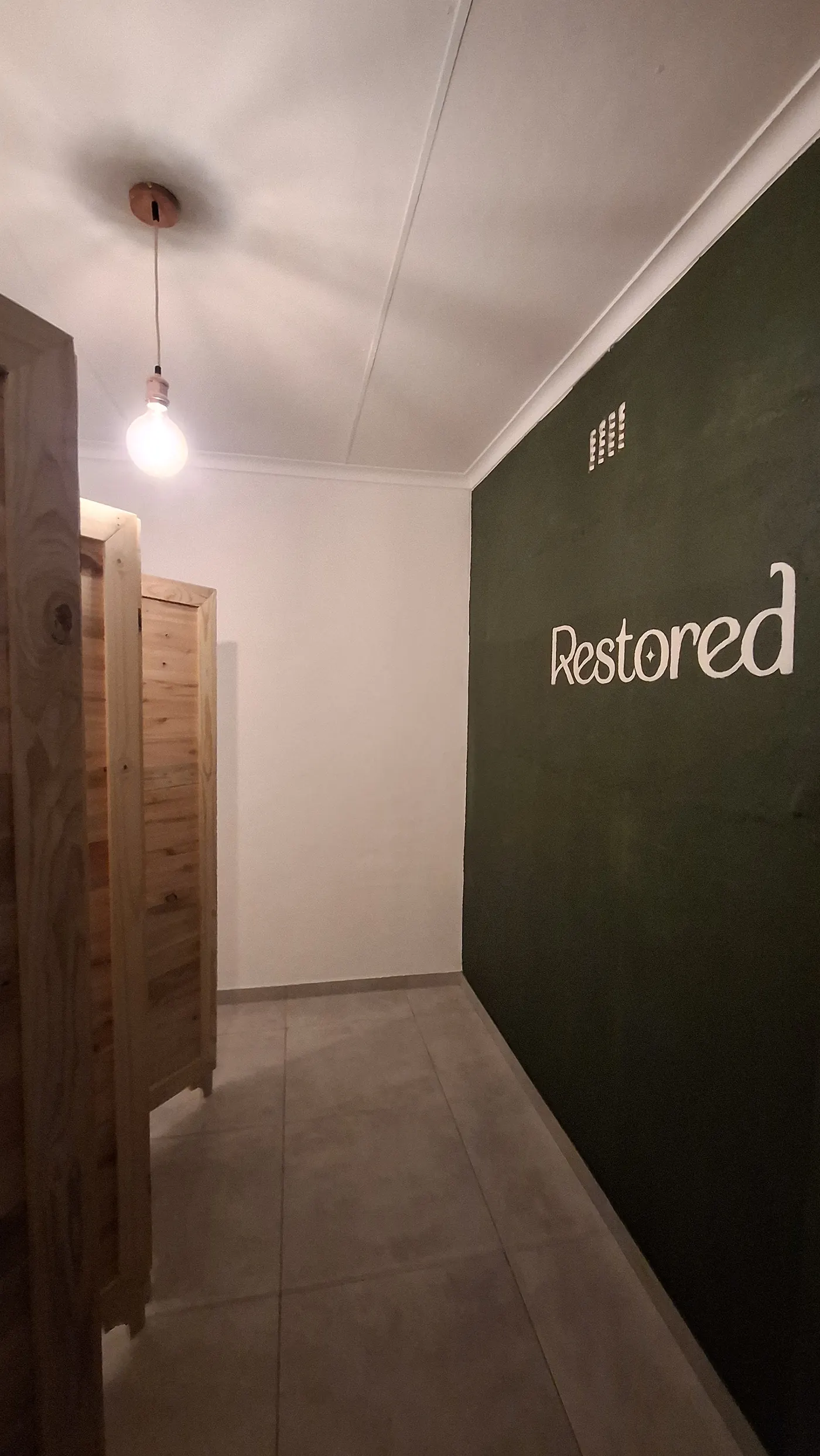 The Restored studio room: deep green wall with the Restored mark, raw pine and warm light